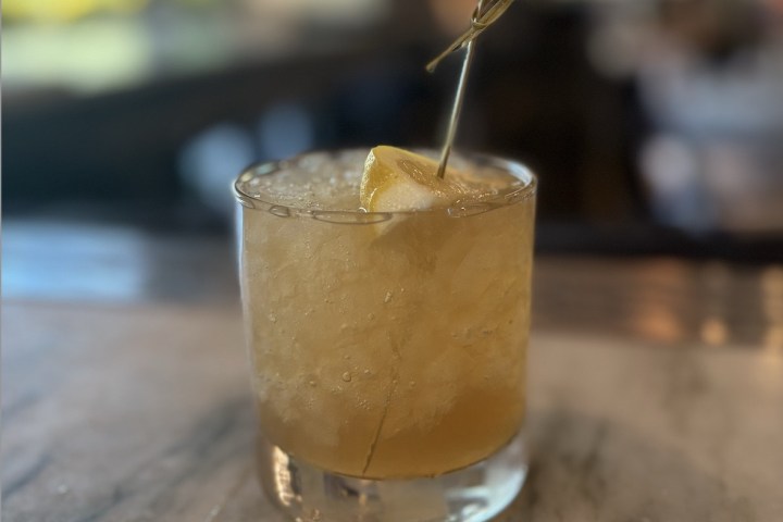 Glass of iced cocktail with lemon slice on a marble surface.